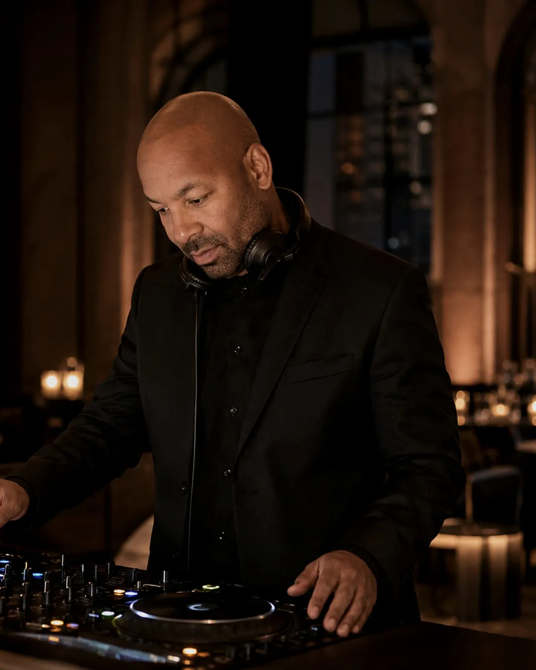 Mike Broom cueing a track at the decks in a candlelit dining room, arched windows behind